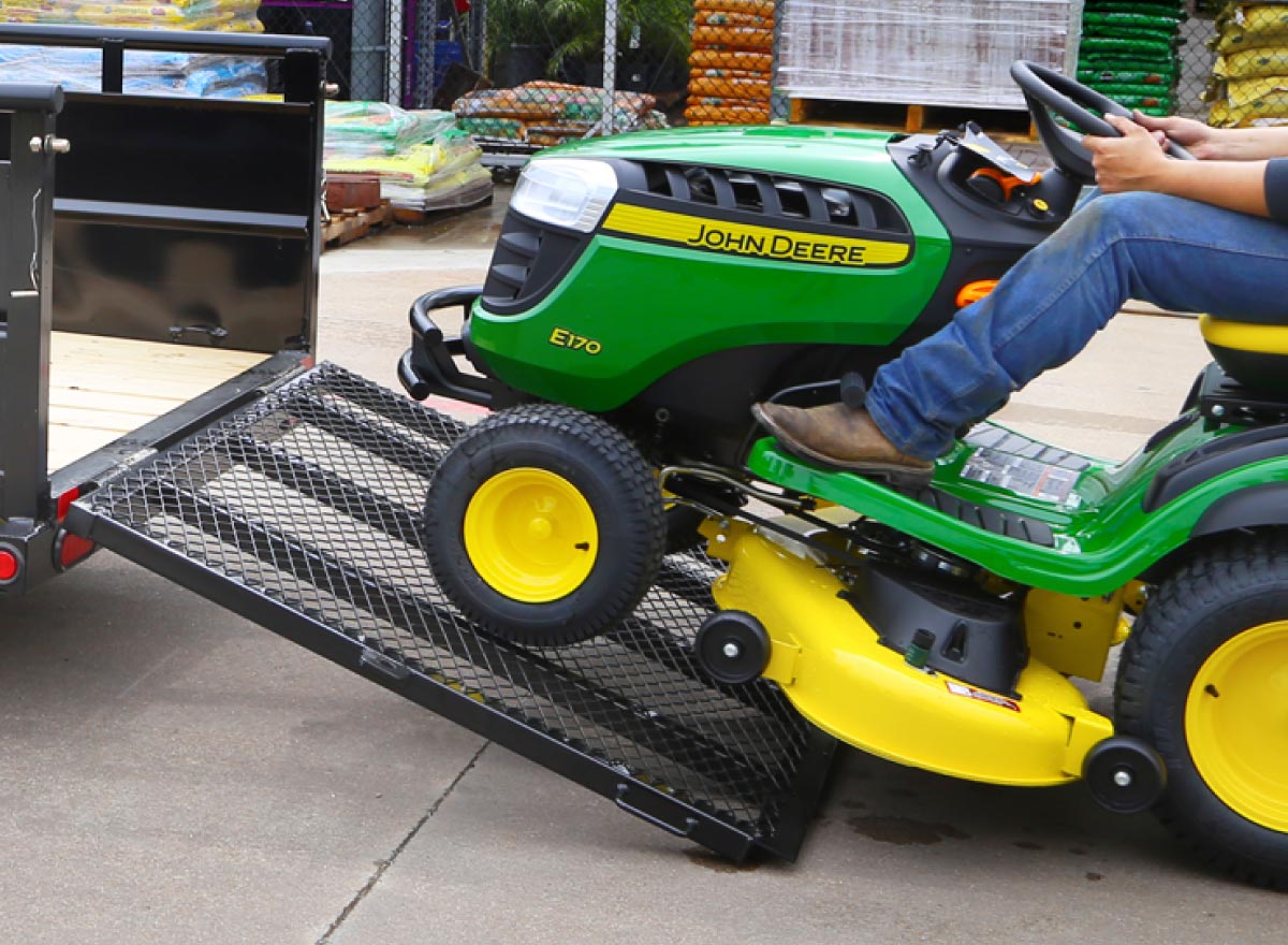 man riding a john deere lawn mower onto a rear trailer rampgate